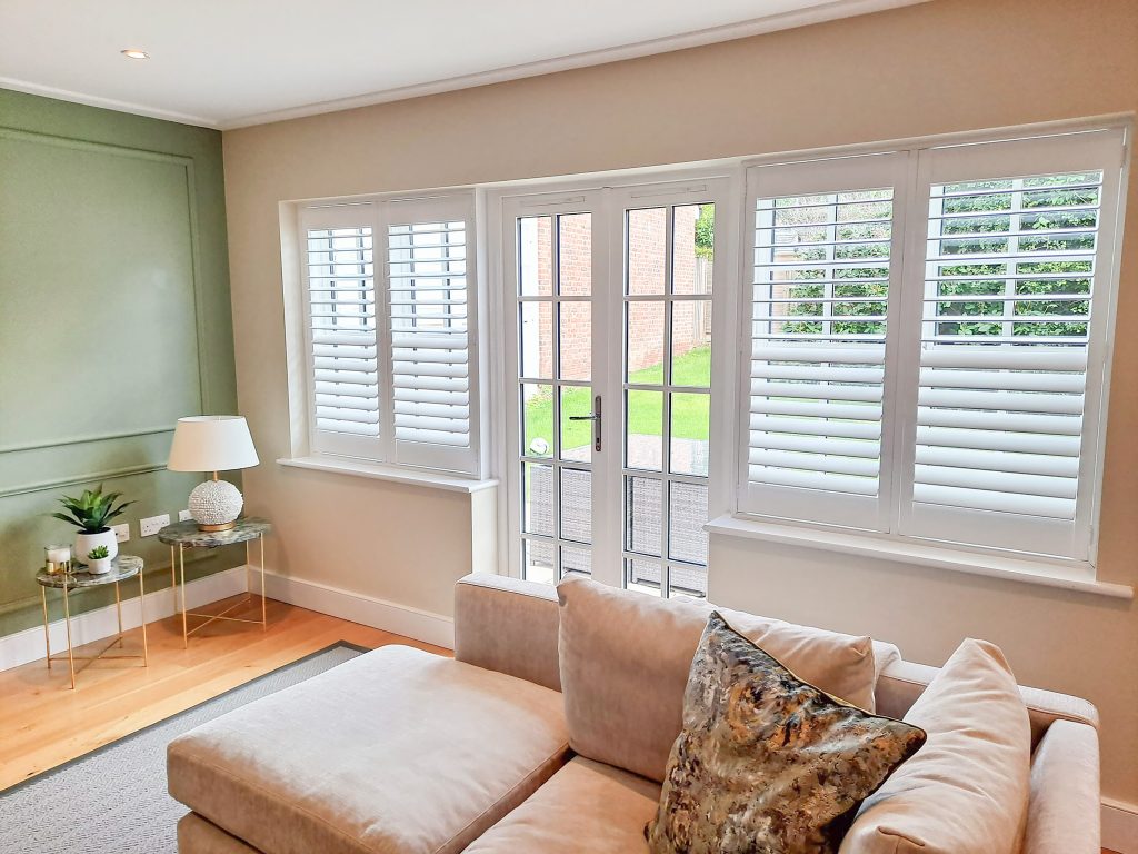 Modern living room with green feature wall, showcasing window shutters for insulation in large windows